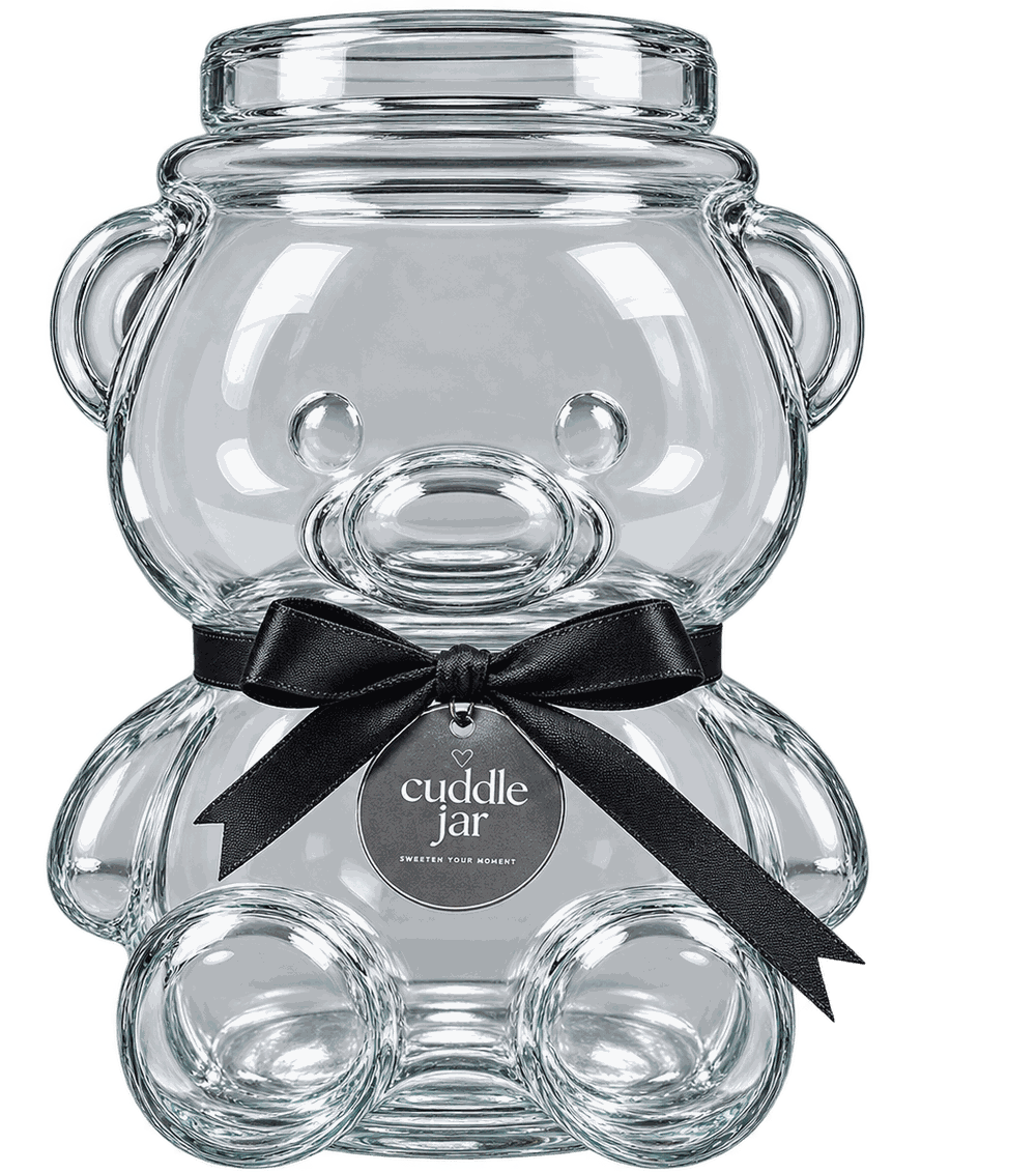 A clear glass jar shaped like a teddy bear, tied with a black satin ribbon and a round Cuddle Jar tag.